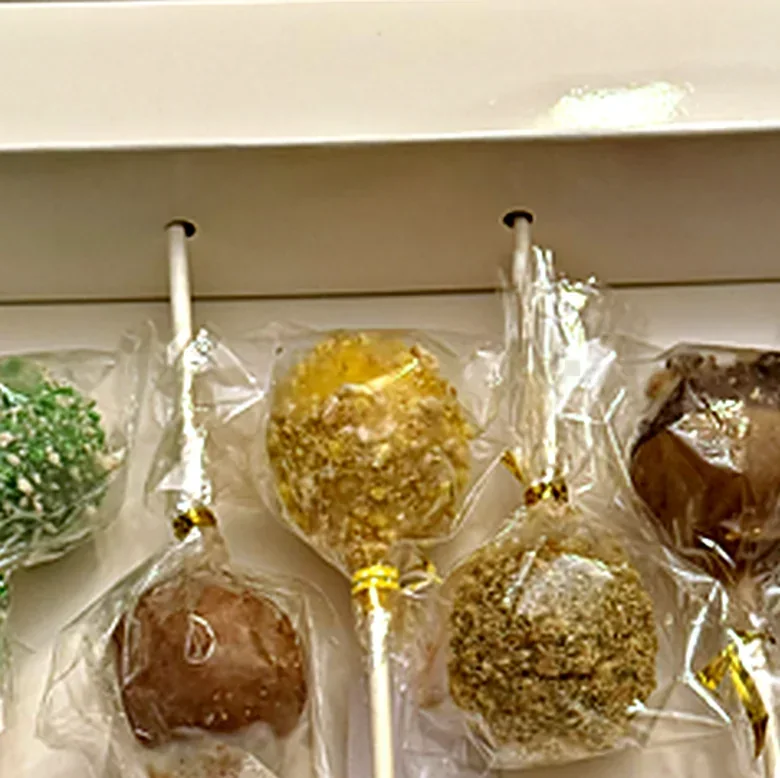 Close up of cake pops sealed in clear bags with gold ties, resting in a box with holes cut for the sticks